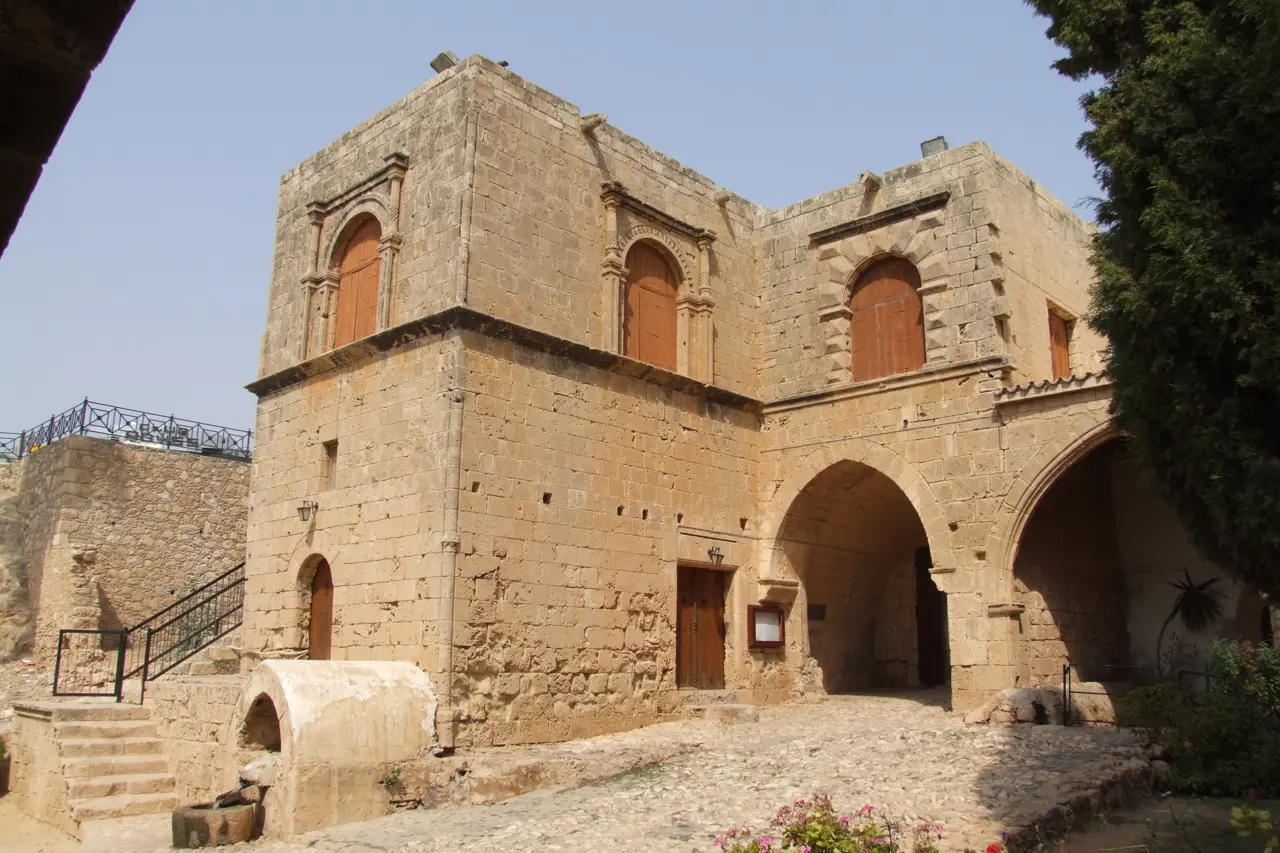Sandstone monastery building with arched windows, an outside staircase and a vaulted passage by a cobbled courtyard