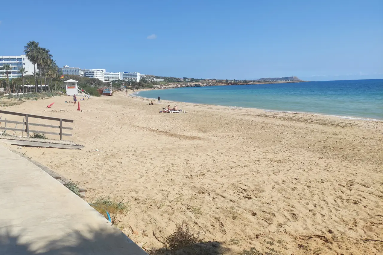 Wide sandy beach with palms and hotels along the shore under a clear sky