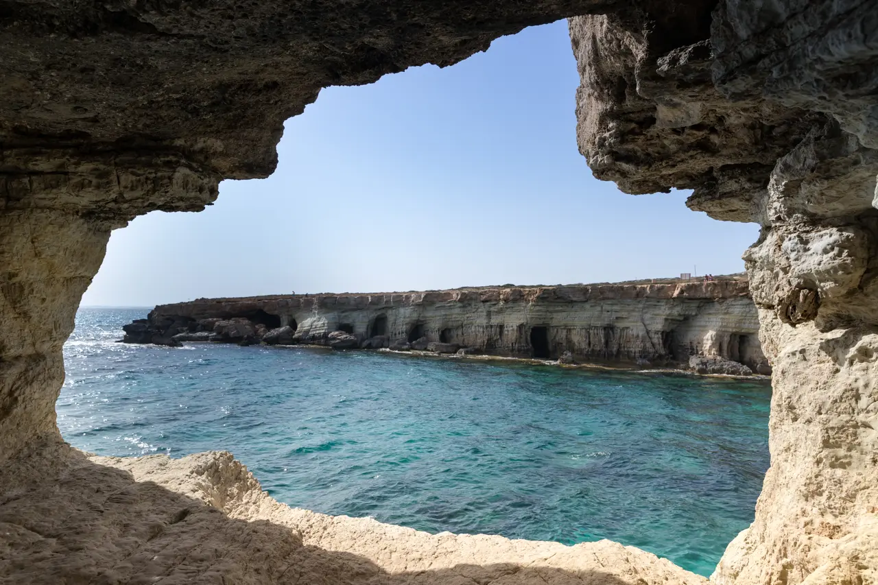 View through a cave opening onto a cliff with more caves along the sea