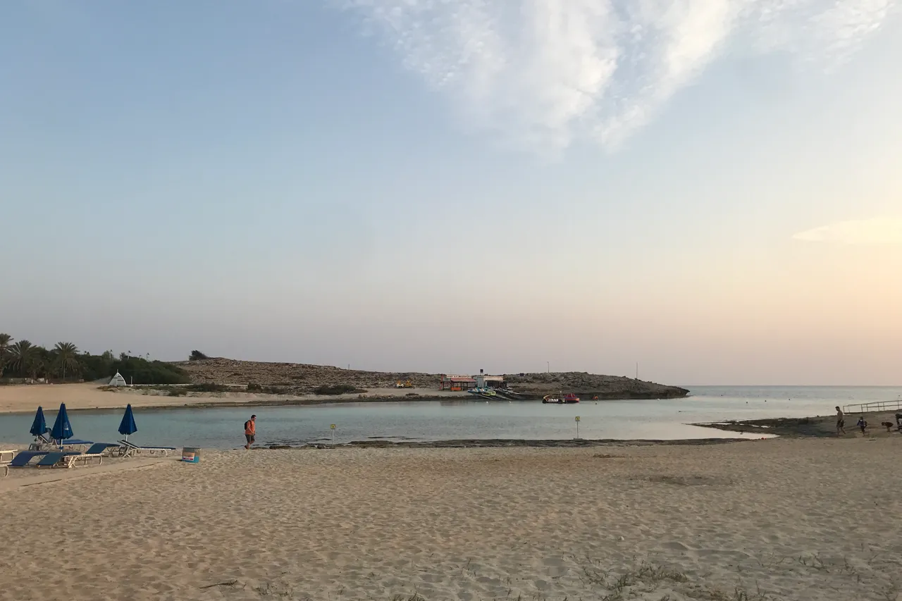 Wide sandy beach at dusk with a few blue sunshades and a person at the water's edge