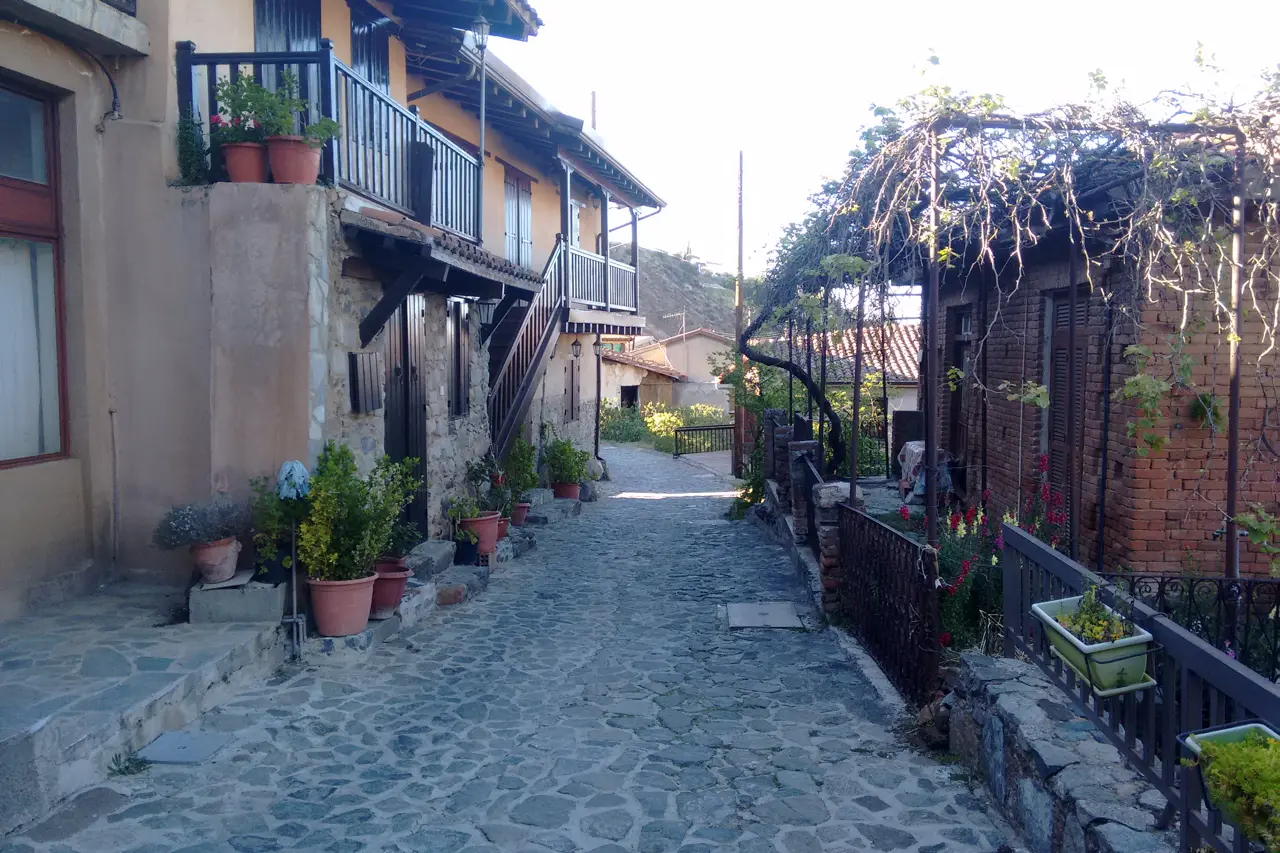 Cobbled lane between old stone houses with a wooden balcony, flower pots and a vine pergola