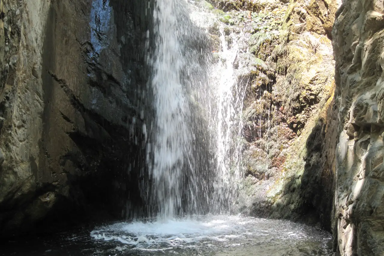A waterfall dropping through a dark rock gorge into a pool, with spray and green moss on the walls