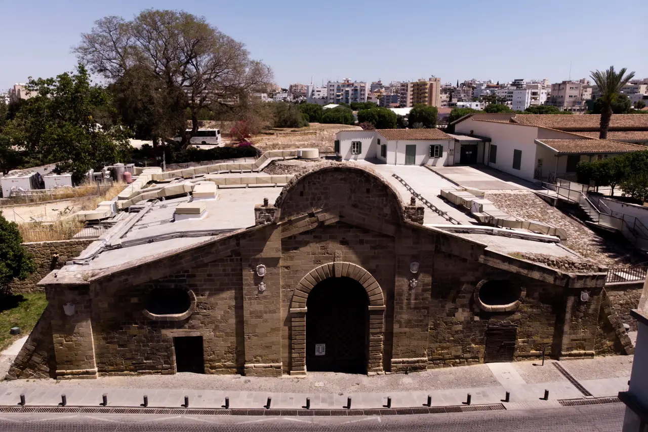 Stone gate with an arched entrance and a flat roof seen from above, with trees and city buildings behind