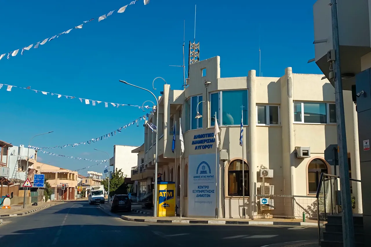 Village street with bunting overhead and a cream-coloured municipal building with flags on the corner
