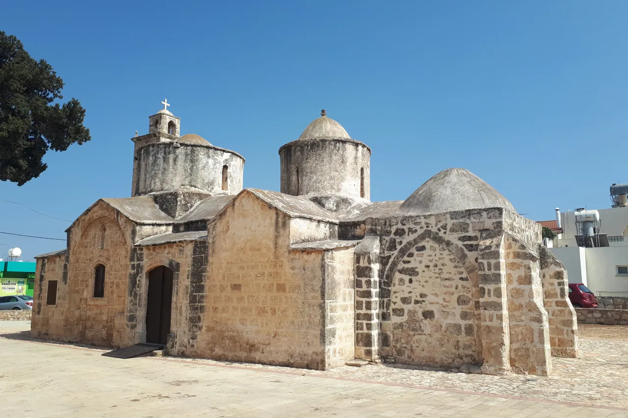 Small stone church with several domes on a cobbled forecourt under a blue sky