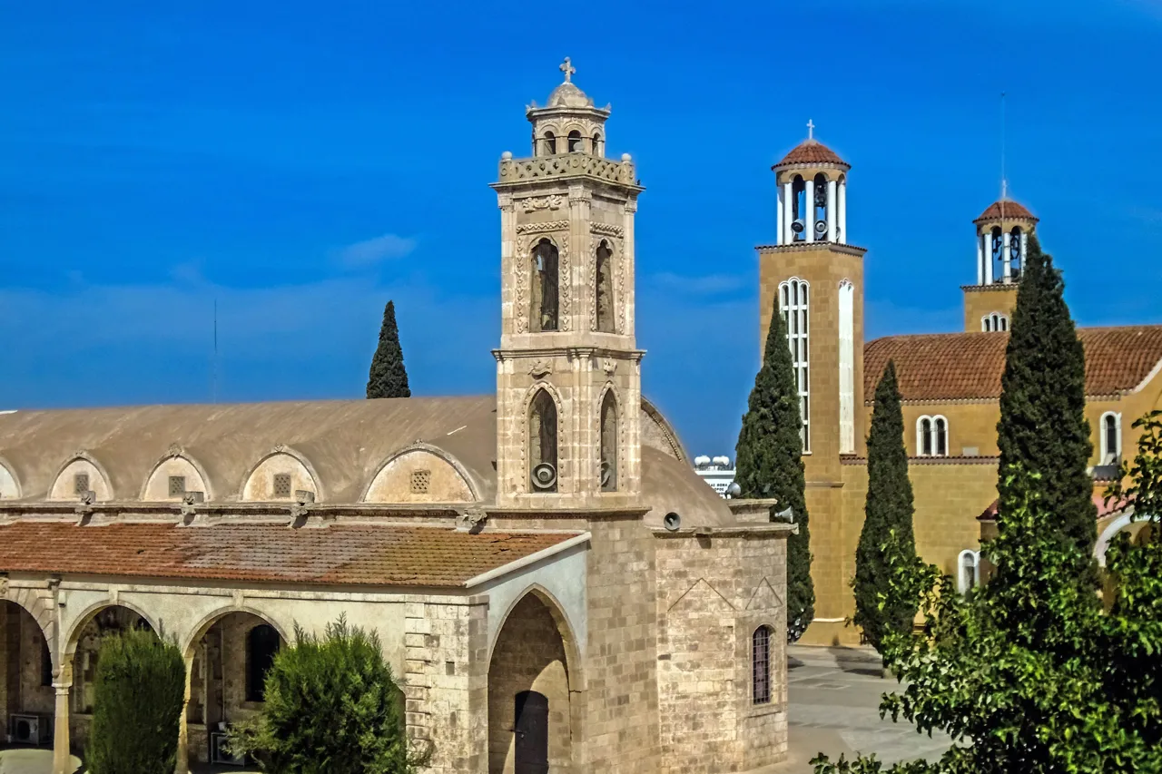 Two sandstone churches with bell towers and tall cypress trees against a deep blue sky