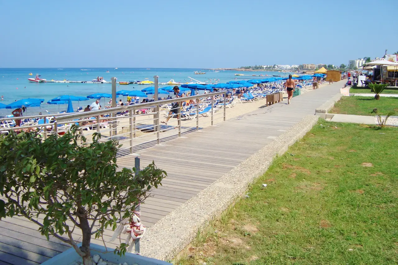 Wooden boardwalk beside a sunbed-lined beach, with a lawn and a café on the right and the sea on the left